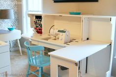 a sewing machine sitting on top of a white desk next to a blue chair in front of a window