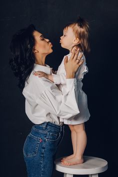 a woman holding a small child up to her face while standing on top of a stool