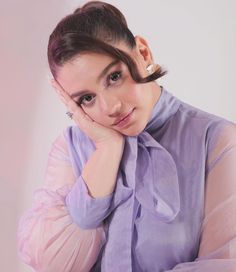 a woman with her hand on her chin, wearing a purple shirt and looking at the camera