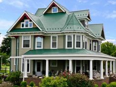 a large house with green roof and white pillars on the front porch is surrounded by greenery