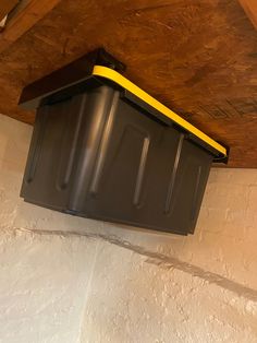 a yellow and black box hanging from the side of a wall under a wooden ceiling