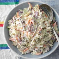 a white bowl filled with coleslaw on top of a striped table cloth next to a fork