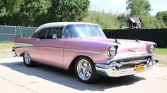 an old pink car is parked on the side of the road in front of a fence