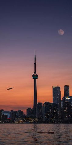 an airplane is flying over the city at night with a full moon in the sky