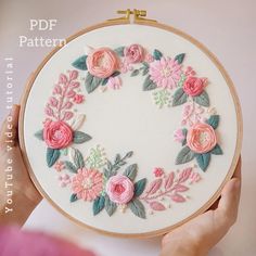 a woman is holding up a embroidery hoop with pink flowers and green leaves on it