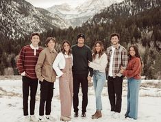 a group of people standing next to each other in the snow with mountains behind them