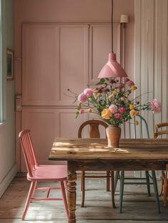 a wooden table topped with pink chairs next to a vase filled with flowers on top of it