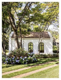 a white house with blue flowers in the front yard