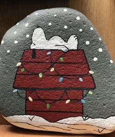 a painted rock with a snoopy christmas scene on it