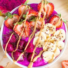 a bowl filled with sliced strawberries and bananas on top of a wooden table next to other fruits