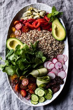 a white plate topped with lots of veggies next to sliced avocado