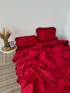 a bed with red sheets and pillows on top of it next to a small table