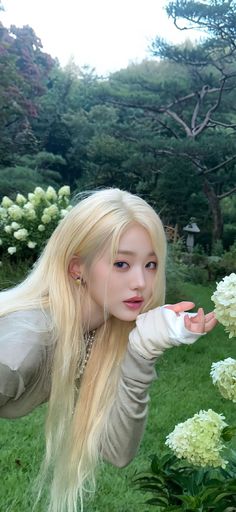 a woman with long blonde hair posing for a photo in front of some white flowers