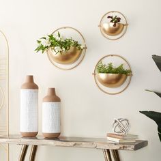 three gold planters are on the wall above a wooden table with two vases