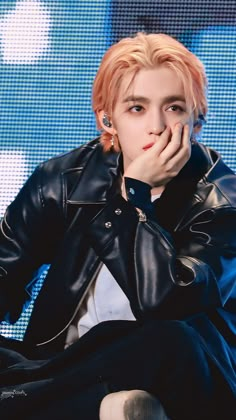 a male in a black leather jacket and white shirt is sitting on a blue chair