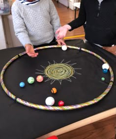 two children are playing with an object made out of yarn and balls on a table