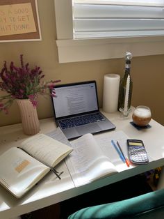 a laptop computer sitting on top of a desk next to an open book and calculator