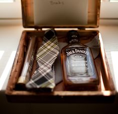 a bottle of jack daniels next to a tie in a wooden box on the floor