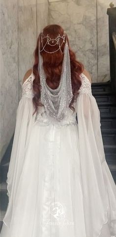 a woman in a white wedding dress walking down some stairs with her veil draped over her head