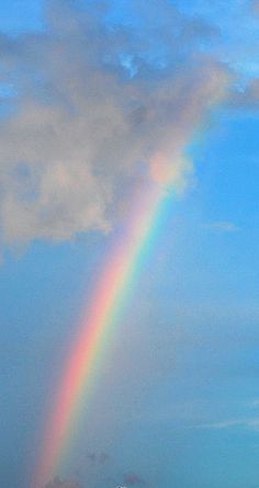 a rainbow in the sky over a beach with people standing on the sand under it