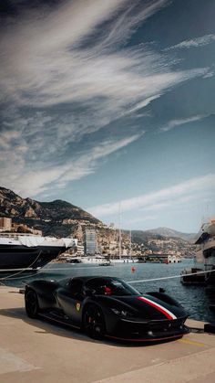 a black sports car parked in front of a large body of water next to a boat