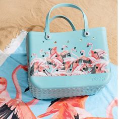 a blue purse sitting on top of a beach towel next to a pink flamingos