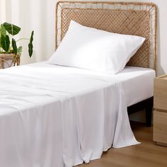 a bed with white sheets and pillows in a room next to a potted plant