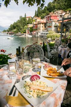 two plates of food on a table with water and buildings in the background