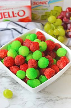 a bowl filled with green and red gummy bears next to some grapes on a counter