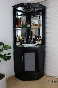 a corner bar with wine glasses and liquor bottles on the top shelf next to a potted plant