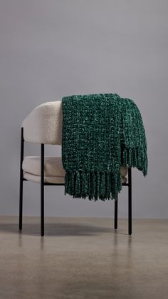 a chair with a green and white blanket on it's back, in front of a gray wall