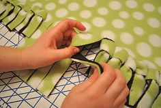 someone cutting fabric with scissors on top of a green and white table cloth that has polka dots