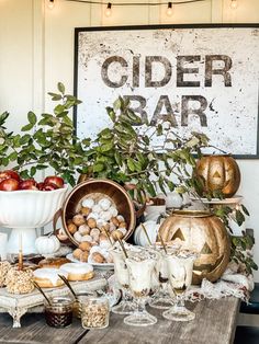 a wooden table topped with lots of desserts and drinks next to a sign that says cider bar