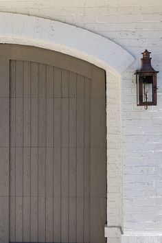 a white brick building with a brown door and light on the side walk next to it