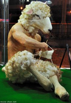 a fake sheep sitting on top of a green carpet next to a glass case filled with yarn