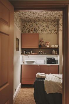 a kitchen with brown cabinets and floral wallpaper on the walls is seen through an open door