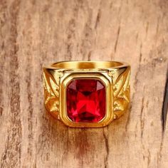 a gold ring with a red stone in the center on top of a wooden table