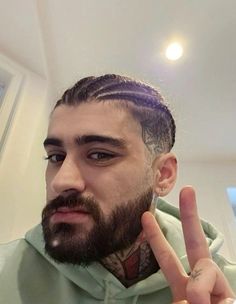 a man with long hair and beard making the peace sign while wearing a green hoodie