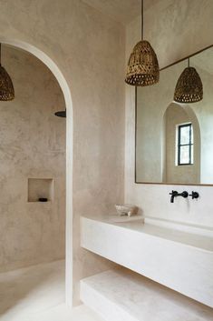 a bathroom with two sinks, mirrors and lights hanging from the ceiling above it is an arched doorway leading to another room