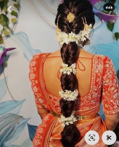 a woman with flowers in her hair wearing an orange sari and braided hairs