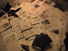 many books are spread out on the floor with drawings and other items scattered around them