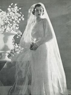 an old photo of a woman wearing a wedding dress and veil with flowers in the background