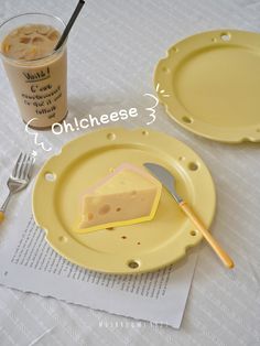 two yellow plates with cheese on them next to a fork and glass filled with liquid