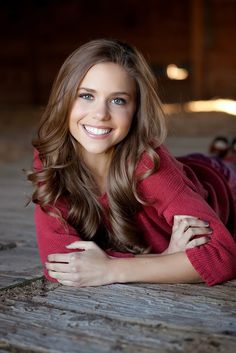 a beautiful young woman laying on the ground in a red sweater smiling at the camera