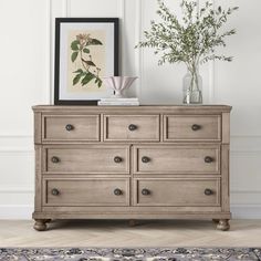 a wooden dresser with drawers and vases on top of it in front of a white wall