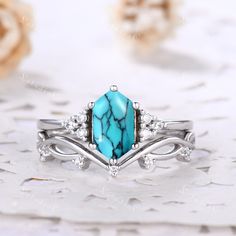 a turquoise stone and diamond ring sitting on top of a white table with flowers in the background