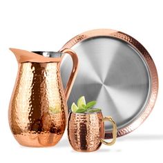 a copper pitcher next to a silver plate and a cup with a mint in it