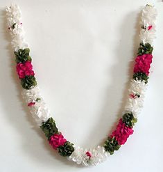 a white and pink flowered necklace is displayed on a white surface with green leaves