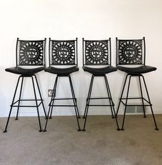 four black metal stools sitting in front of a white wall