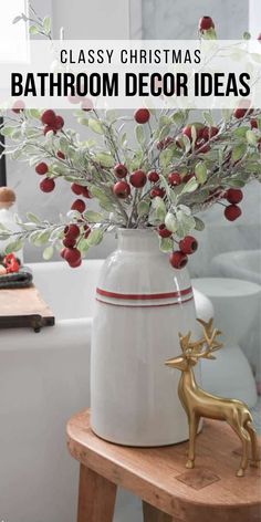 a white vase with red berries and greenery in it sitting on a wooden table